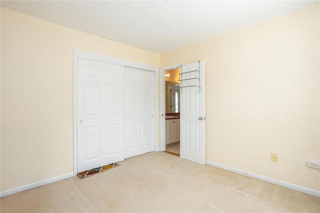 unfurnished bedroom featuring a closet, baseboards, and light colored carpet