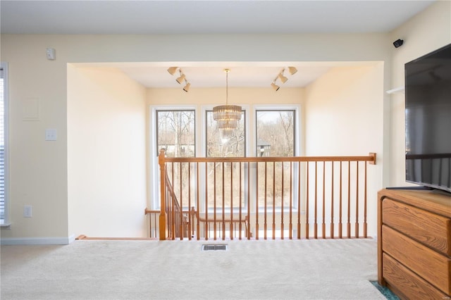 corridor featuring a notable chandelier, track lighting, carpet, and visible vents