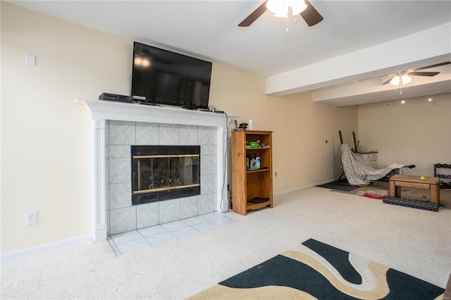 living room featuring a tiled fireplace, baseboards, ceiling fan, and carpet floors