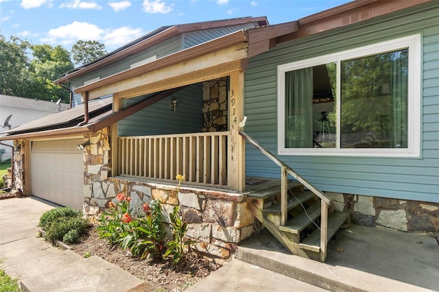 entrance to property with concrete driveway, an attached garage, a porch, and stone siding