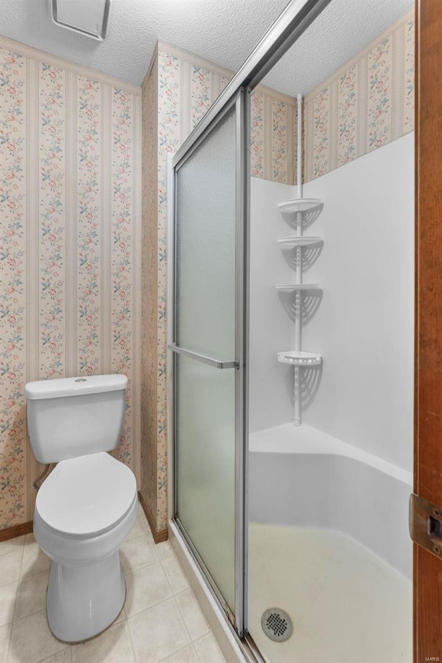 bathroom featuring tile patterned floors, toilet, a stall shower, a textured ceiling, and wallpapered walls