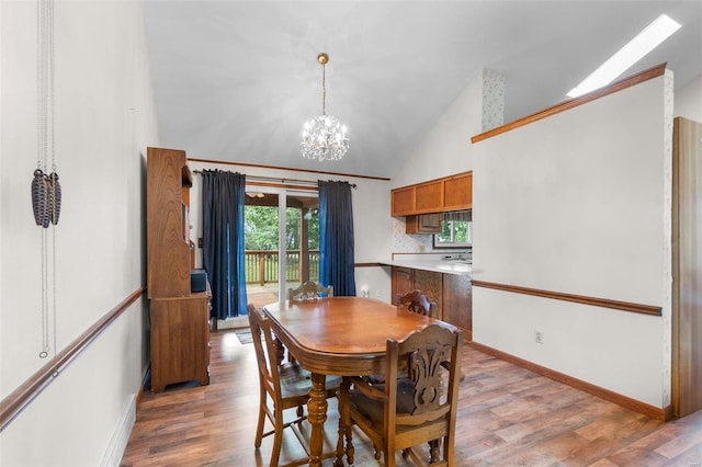 dining room with a notable chandelier, baseboards, light wood-type flooring, and high vaulted ceiling