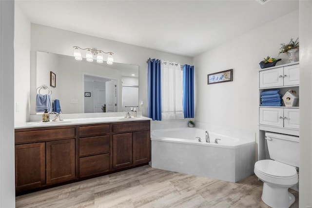 bathroom with wood finished floors, double vanity, a sink, a garden tub, and toilet