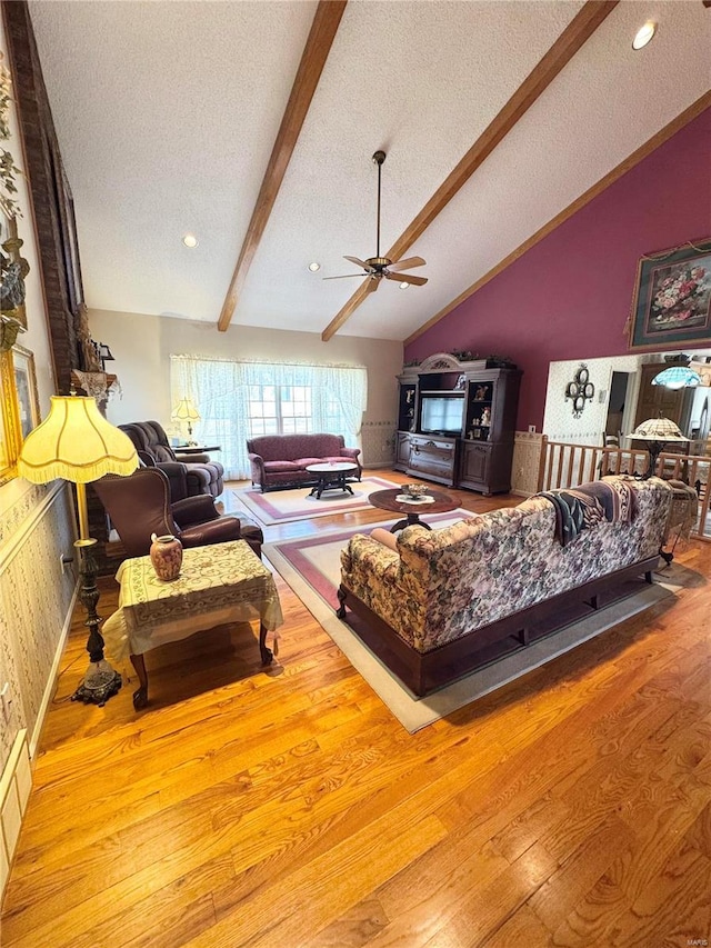 living area with ceiling fan, a textured ceiling, wood finished floors, and vaulted ceiling with beams