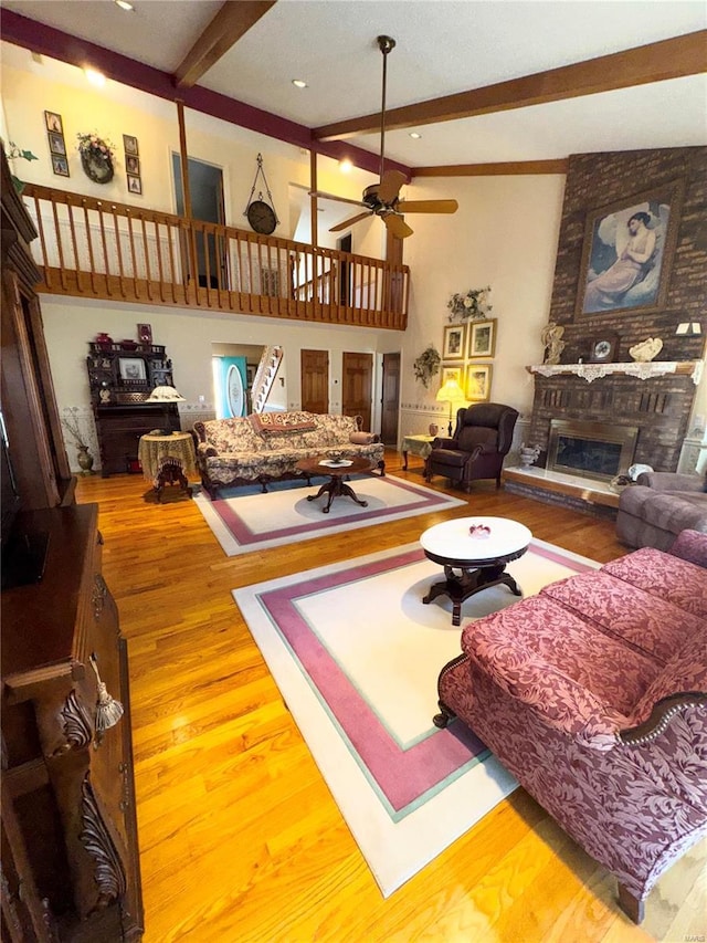 living room featuring beam ceiling, a ceiling fan, wood finished floors, a high ceiling, and a fireplace