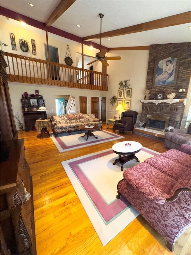 living room with a ceiling fan, wood finished floors, beam ceiling, a towering ceiling, and a brick fireplace