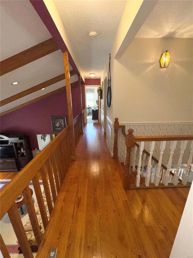 hall with a textured ceiling, vaulted ceiling with beams, and wood finished floors