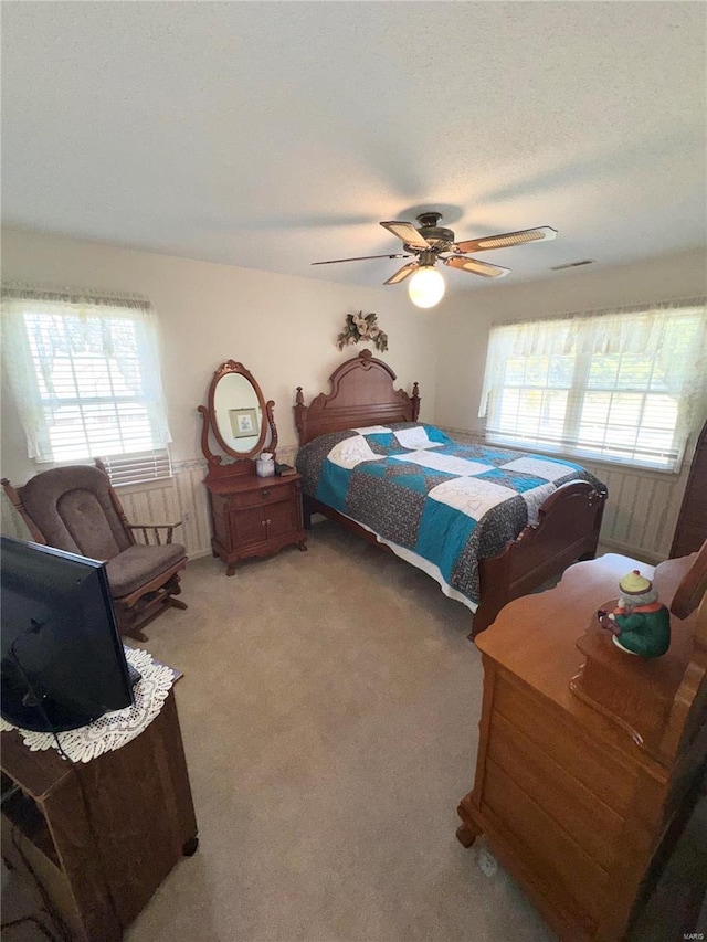 bedroom with light carpet, visible vents, multiple windows, and a ceiling fan