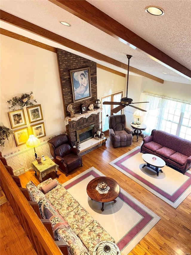 living area with a fireplace, a textured ceiling, lofted ceiling with beams, and wood finished floors