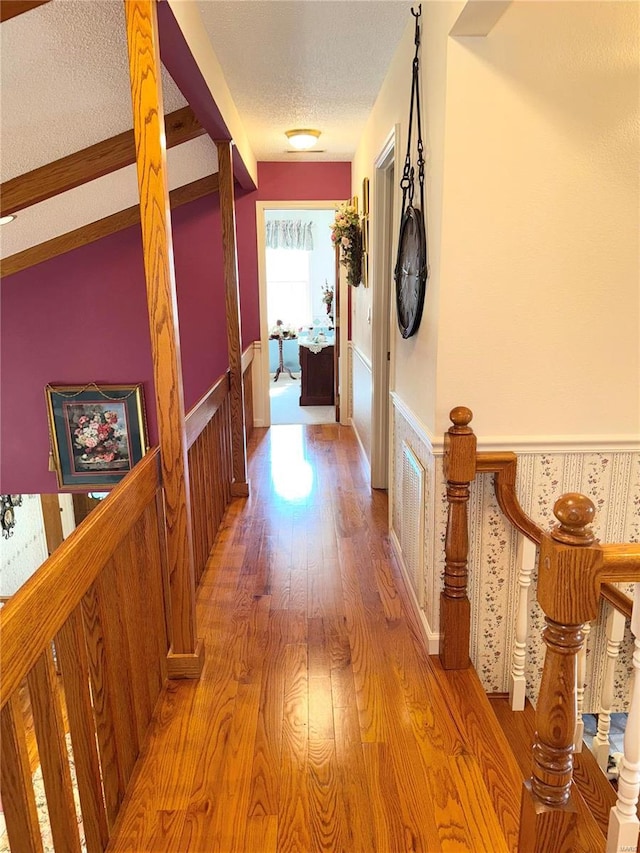 hallway featuring a wainscoted wall, a textured ceiling, and light wood-style floors