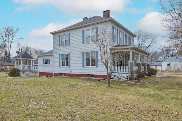 view of front facade with a front yard, a porch, and a chimney