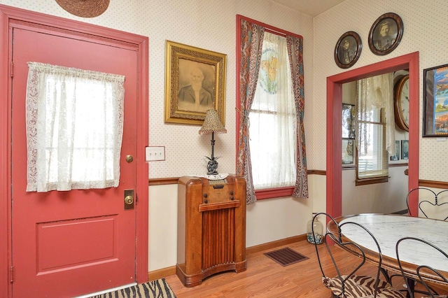 foyer entrance with visible vents, baseboards, light wood-style flooring, and wallpapered walls