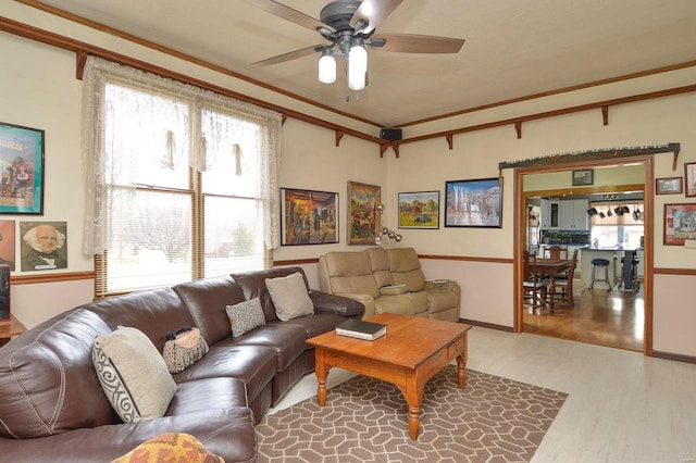 living room featuring light wood-style floors, a ceiling fan, and crown molding