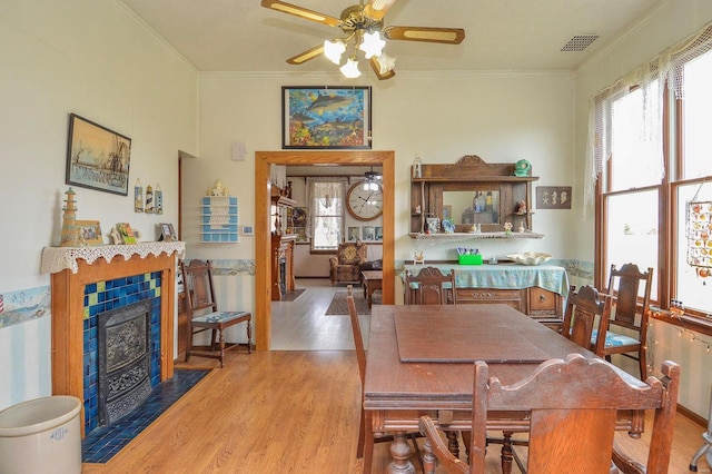 dining room featuring visible vents, crown molding, ceiling fan, a fireplace, and wood finished floors