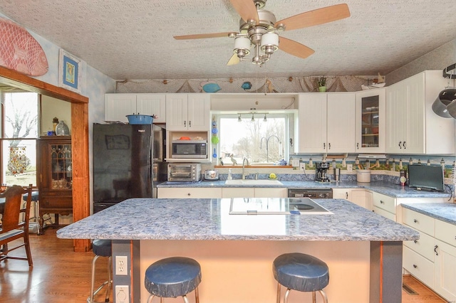 kitchen featuring stainless steel microwave, a kitchen breakfast bar, freestanding refrigerator, and a sink