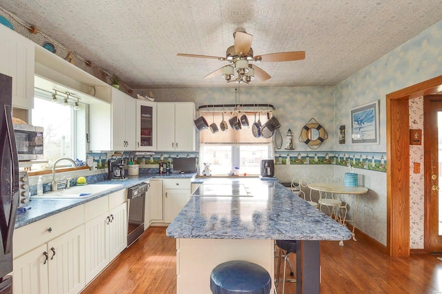 kitchen with wallpapered walls, ceiling fan, a sink, dishwasher, and black electric cooktop