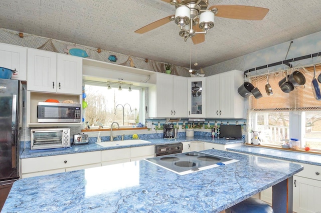 kitchen with freestanding refrigerator, a sink, cooktop, stainless steel microwave, and a wealth of natural light