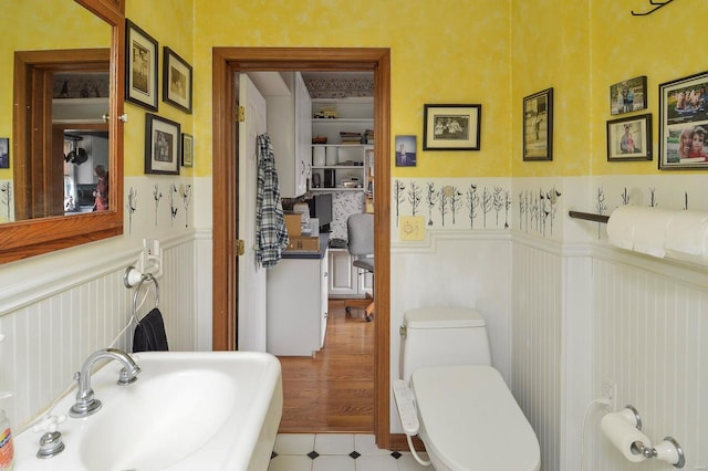 half bath featuring a wainscoted wall, toilet, and a sink