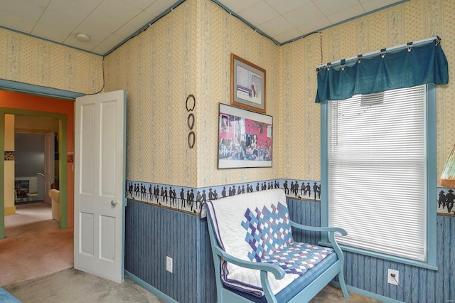 living area featuring wallpapered walls, carpet, and a wainscoted wall