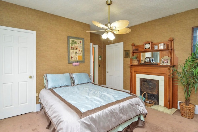 carpeted bedroom with wallpapered walls, a textured ceiling, ceiling fan, and a tile fireplace