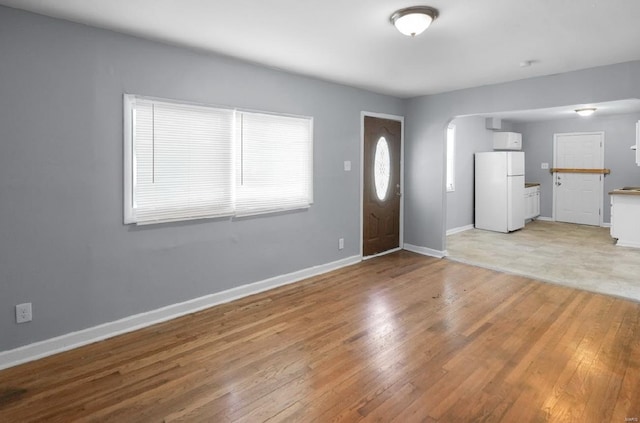 entryway with arched walkways, baseboards, and light wood-style floors