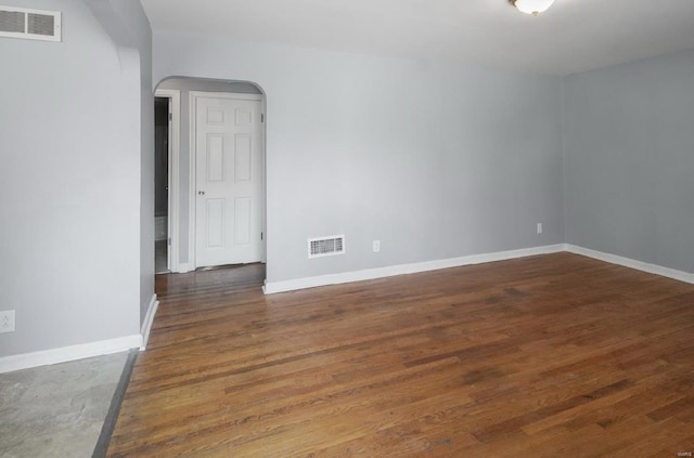 spare room featuring arched walkways, visible vents, baseboards, and wood finished floors