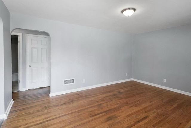 empty room featuring visible vents, arched walkways, baseboards, and wood finished floors