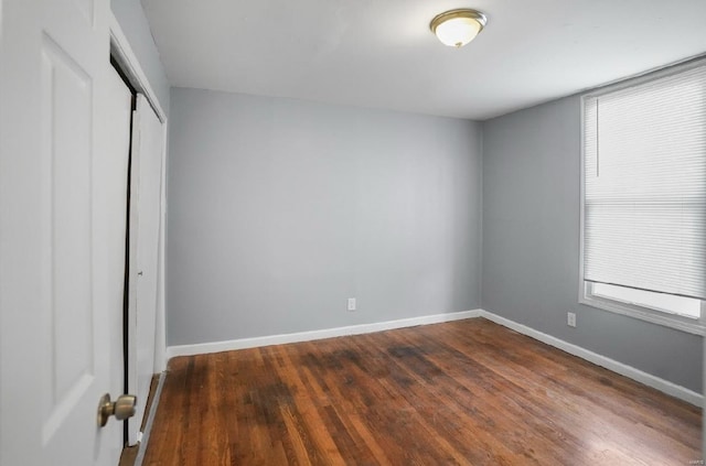 unfurnished bedroom with a closet, baseboards, and dark wood-style floors