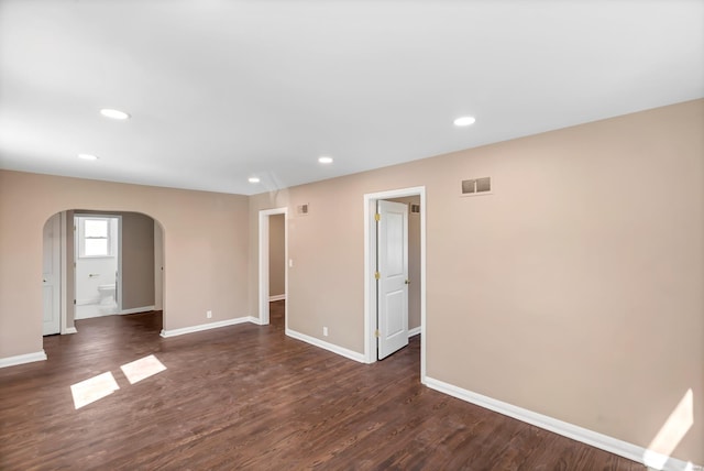 spare room with baseboards, visible vents, recessed lighting, arched walkways, and dark wood-type flooring