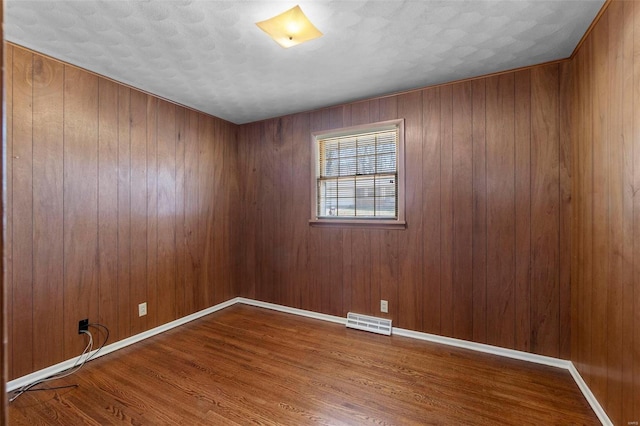 spare room featuring wooden walls, wood finished floors, visible vents, and baseboards