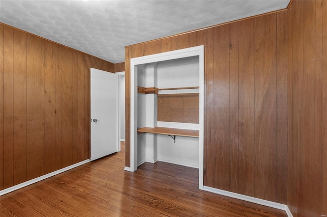 unfurnished bedroom featuring wooden walls, baseboards, and wood finished floors