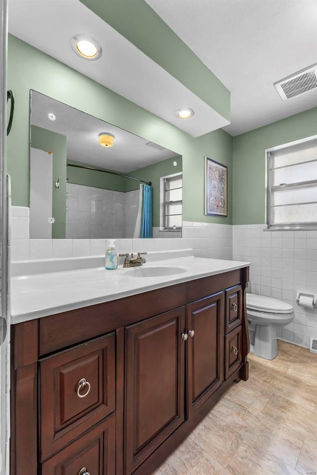 bathroom featuring visible vents, a wainscoted wall, toilet, vanity, and tile walls