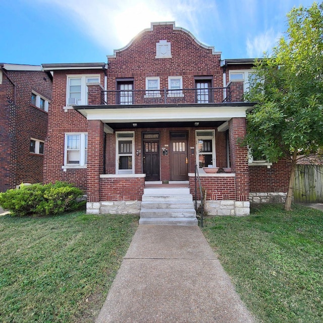 view of property featuring a front lawn, a balcony, covered porch, and brick siding