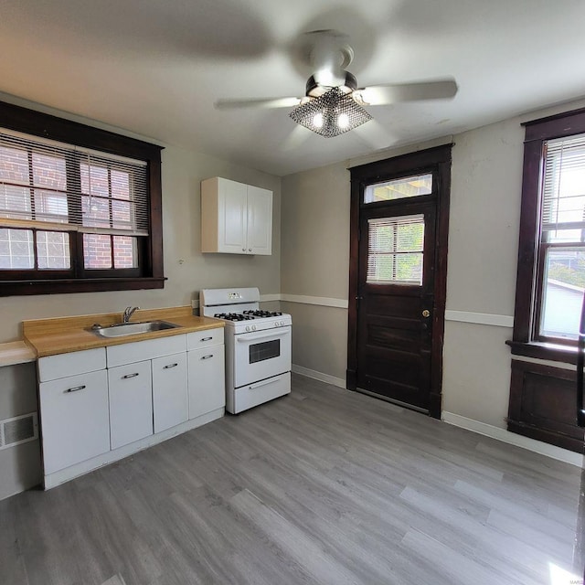 kitchen with ceiling fan, white gas range, white cabinetry, and a sink