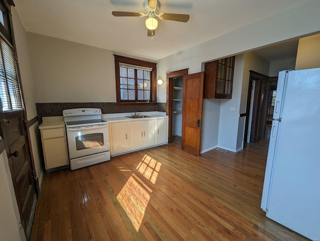 kitchen with light countertops, wood finished floors, white appliances, a ceiling fan, and a sink