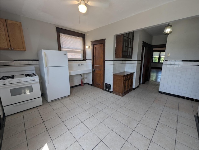 kitchen featuring white appliances, light tile patterned floors, a wainscoted wall, ceiling fan, and tile walls