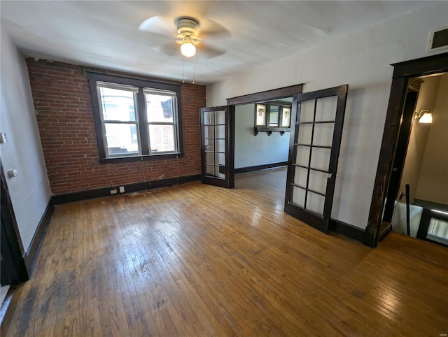 empty room featuring hardwood / wood-style floors, baseboards, brick wall, and ceiling fan