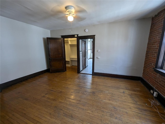 empty room with dark wood-type flooring, baseboards, brick wall, and ceiling fan