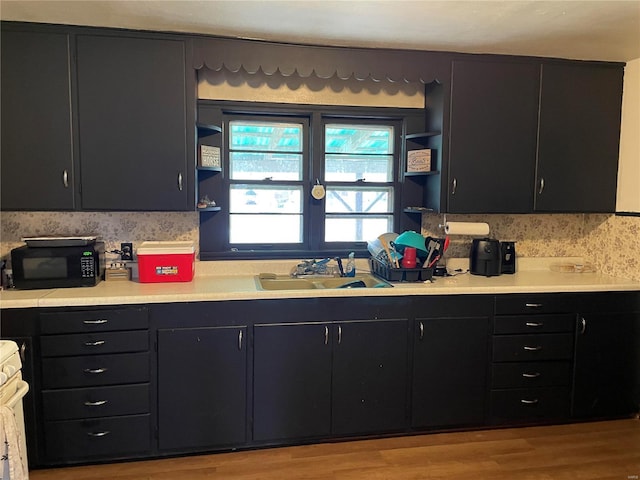 kitchen with open shelves, dark cabinetry, black microwave, and a sink