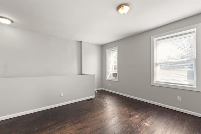 spare room with dark wood finished floors, plenty of natural light, visible vents, and baseboards