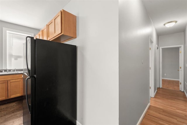 kitchen with a sink, baseboards, wood finished floors, and freestanding refrigerator