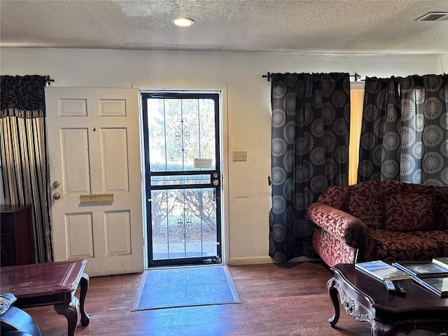 entryway with visible vents, baseboards, a textured ceiling, and wood finished floors