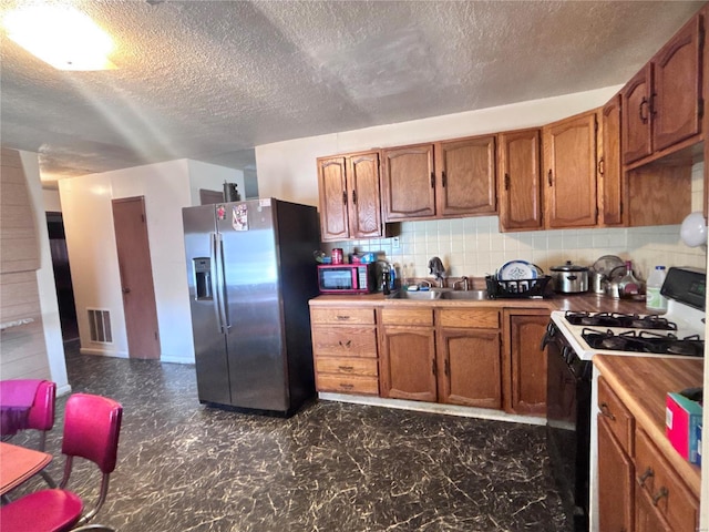 kitchen with visible vents, backsplash, stainless steel fridge with ice dispenser, black gas range, and brown cabinetry