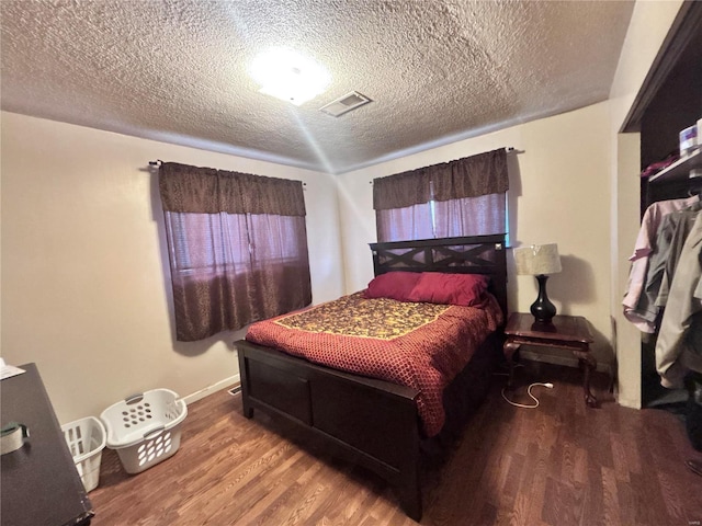 bedroom featuring visible vents, baseboards, a textured ceiling, and wood finished floors