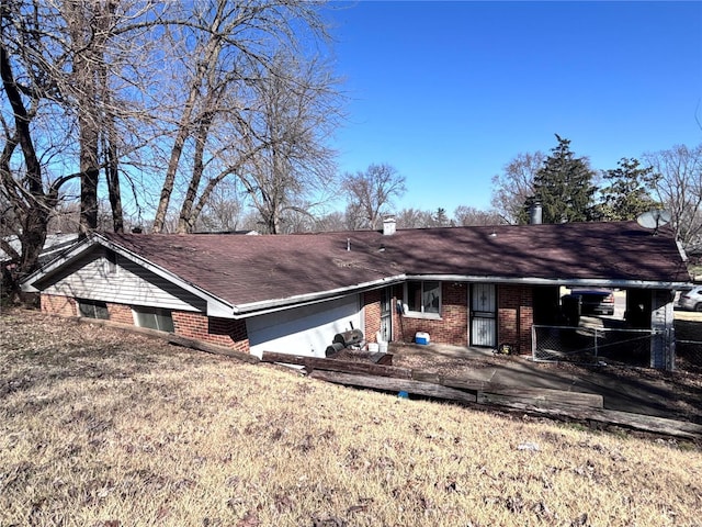 back of house with brick siding, a lawn, and roof with shingles