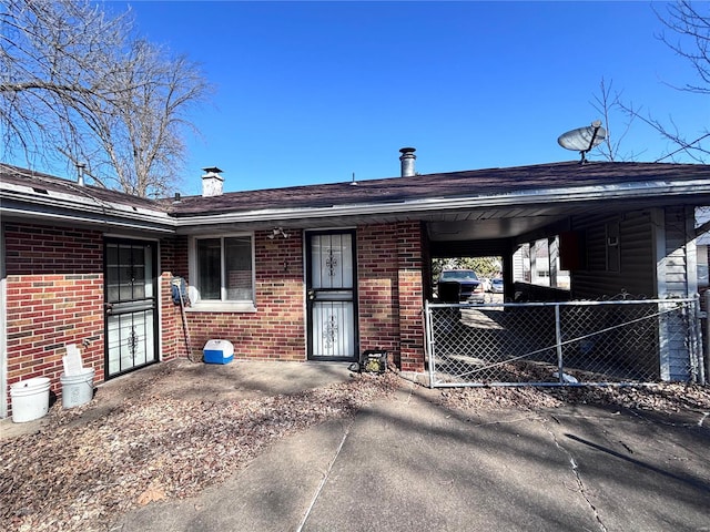 rear view of house with brick siding, a chimney, fence, and a carport