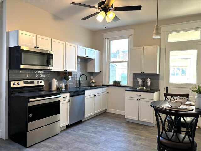 kitchen with a sink, tasteful backsplash, dark countertops, stainless steel appliances, and ceiling fan