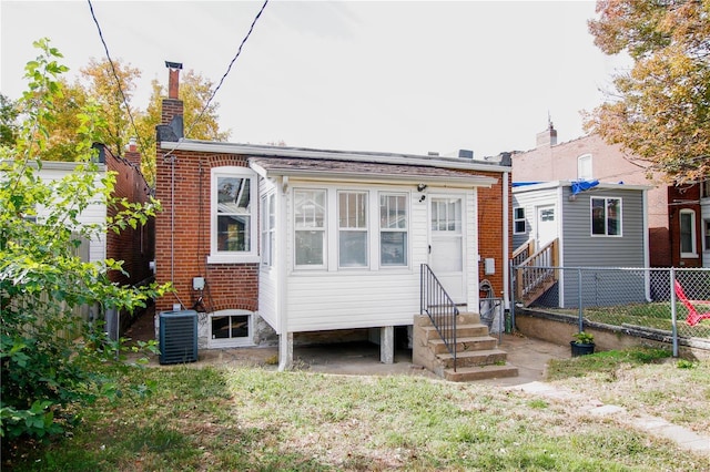 rear view of house with central air condition unit, entry steps, fence, brick siding, and a chimney