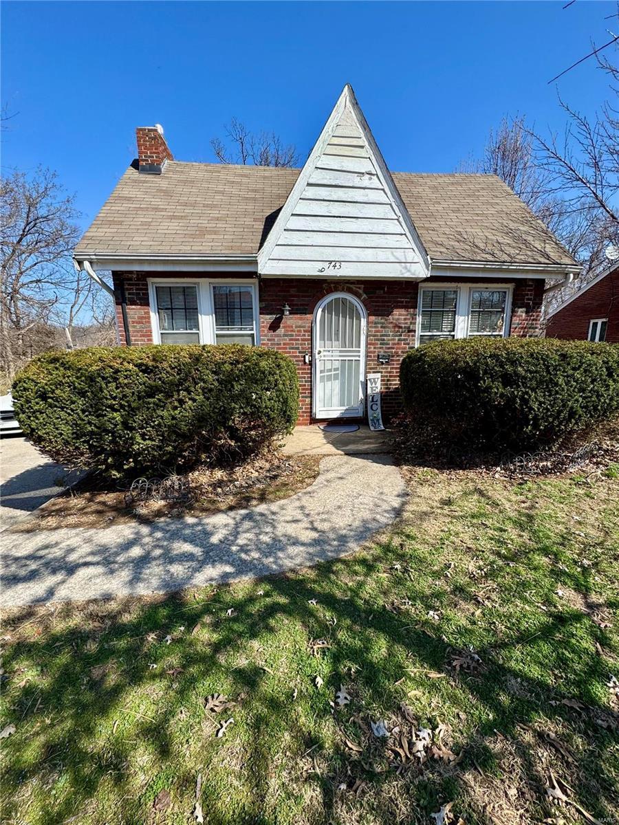 view of front of property featuring brick siding, a chimney, and a front lawn