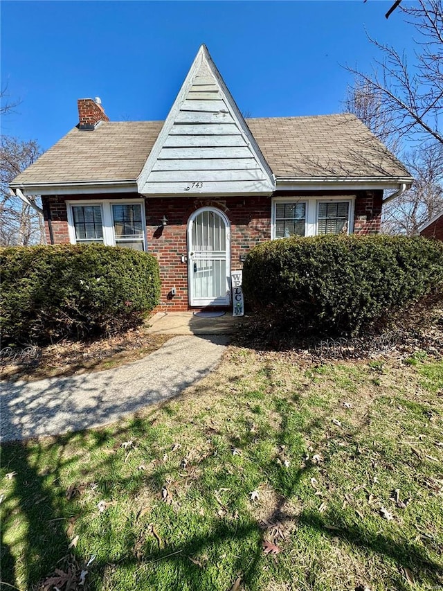 view of front of house with a front lawn, brick siding, and a chimney